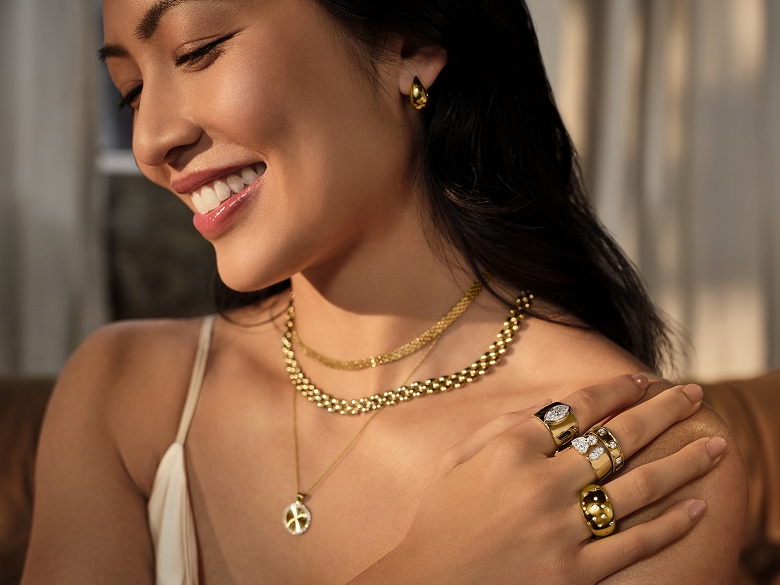An image of a female model wearing yellow gold necklaces, rings and a set of earrings. Shop bold gold.